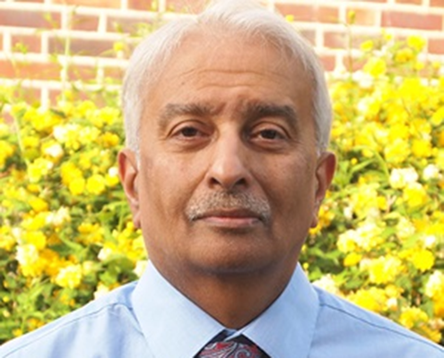 Photo of Krish, a man with short hair and a moustache, standing in front of some greenery