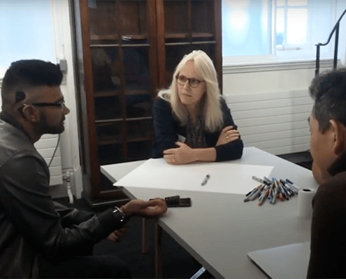 3 people sitting around a desk with pens and paper on the table