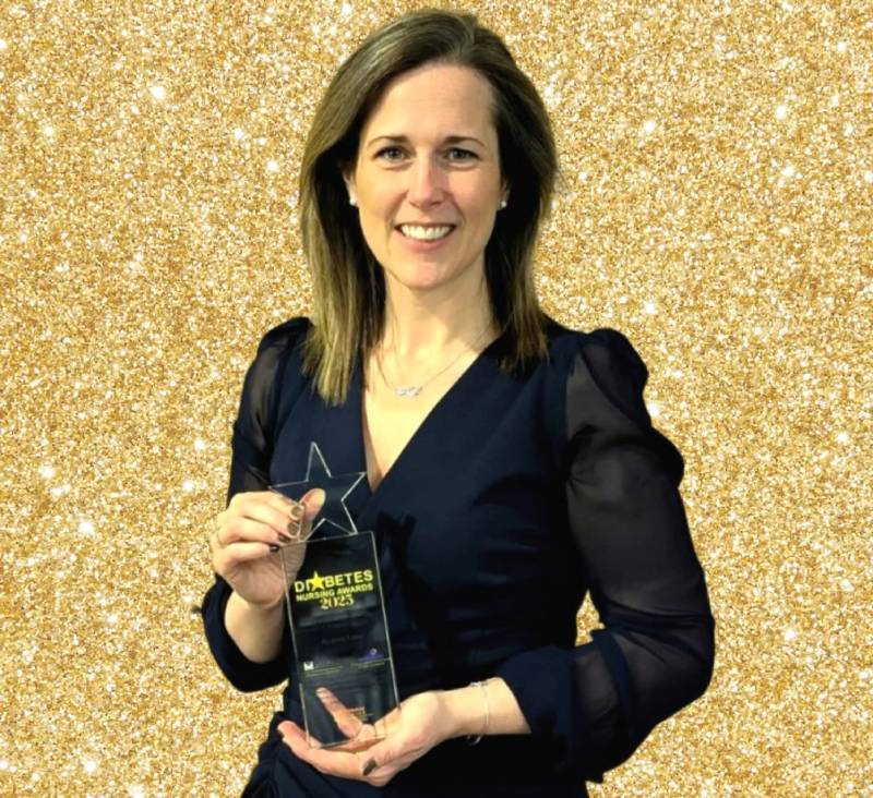 Woman in a black dress smiling holding an award, looking at the camera