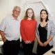 Three people in a hospital clinic room standing smiling at the camera