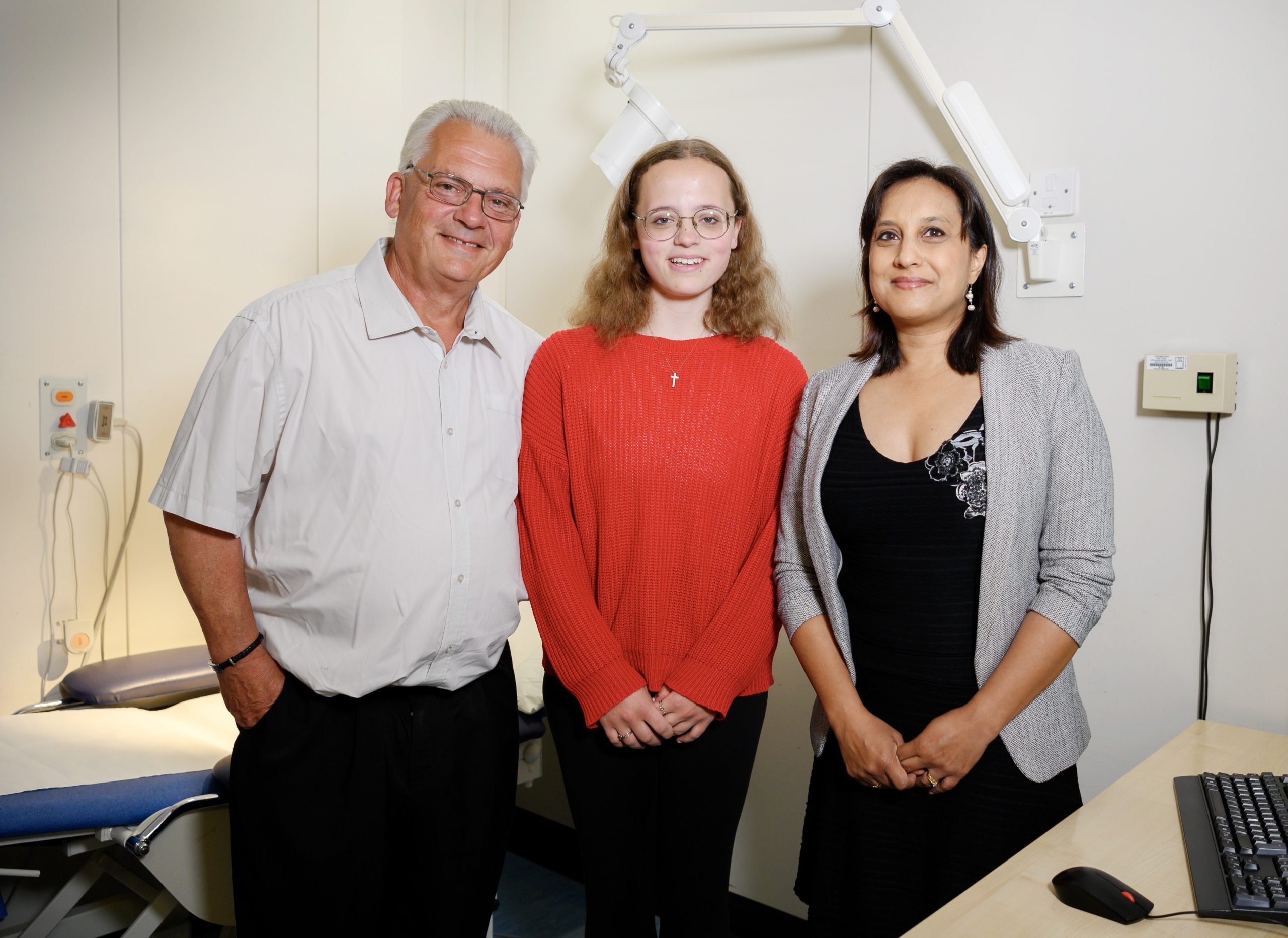 Three people in a hospital clinic room standing smiling at the camera