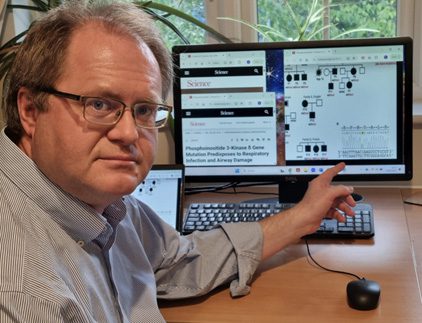 man sitting at a desk with a PC turning back to look the the camera and pointing towards something on the screen