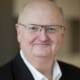 Man wearing a suit and glasses looking at the screen smiling