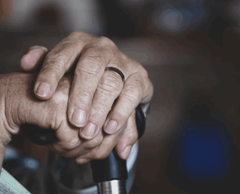 Elderly person's set of hands resting on a walking stick.