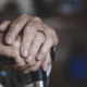 Elderly person's set of hands resting on a walking stick.