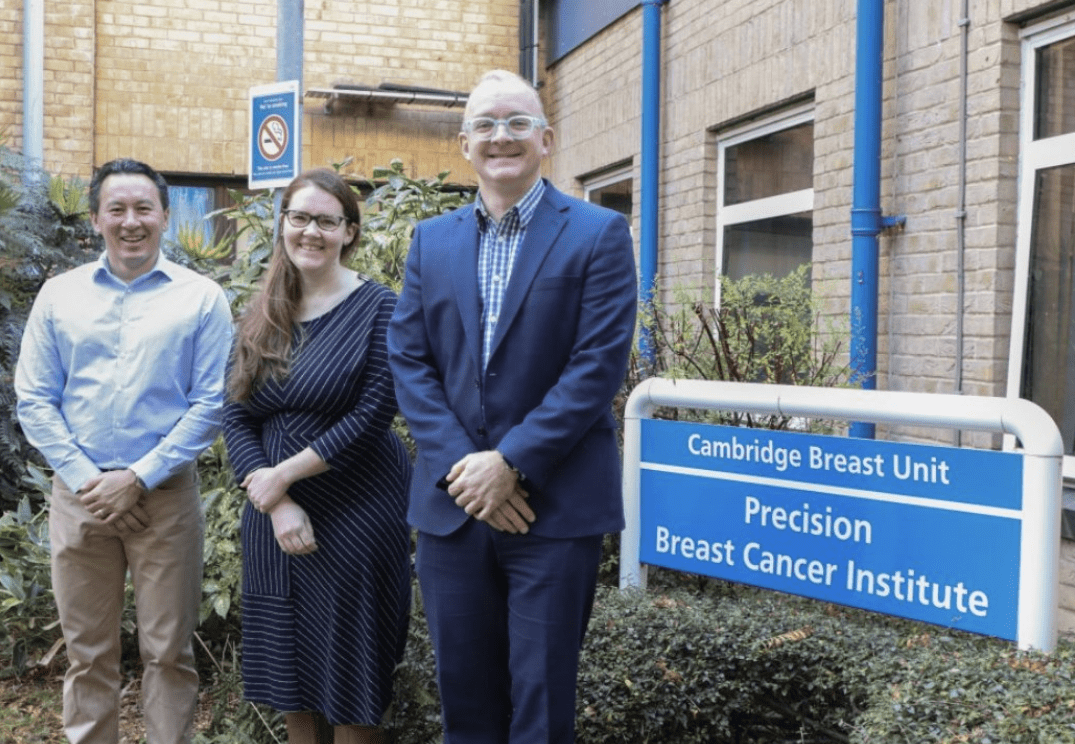 Three people standing outside the Cambridge Breast Unit looking at the camera smiling
