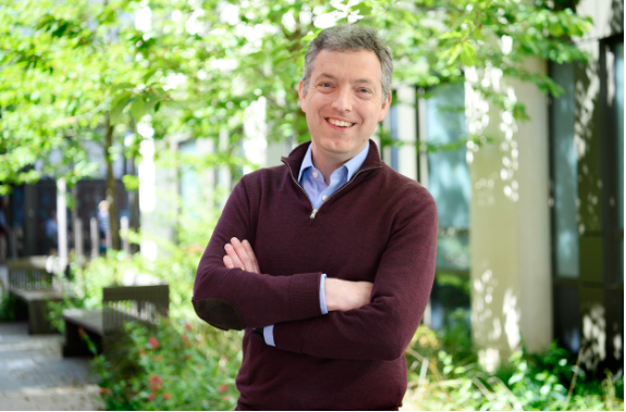 Man in a purple jumper standing under a tree smiling