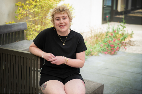 Woman in a black t-shirt and shorts, sitting on a bench, looking at the camera smiling